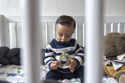 Curious cute little baby sitting in crib and looking down in light room in daytime