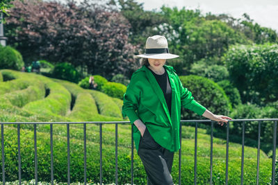 A portrait of one girl in a straw hat pulled halfway down her face stands in the botanical garden