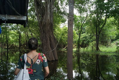 Rear view of woman standing amidst trees in forest