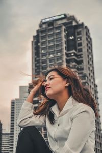 Portrait of young woman looking away against city