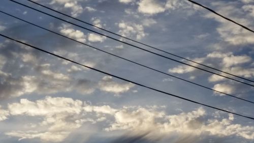 Low angle view of power lines against cloudy sky