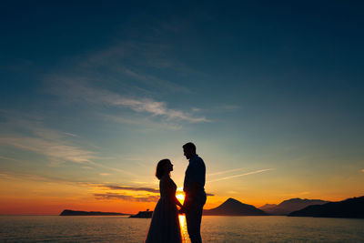 Silhouette woman standing by sea against sky during sunset