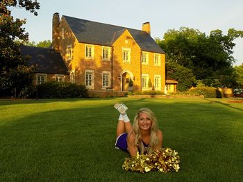 Young woman smiling while standing by lawn against building