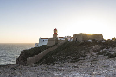 Lighthouse on cliff by sea against clear sky