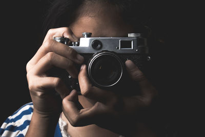 Close-up of girl photographing with camera against black background