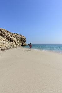 Woman alone at a wild beach of ras al jinz and going to swim in the ocean, sultanate of oman.
