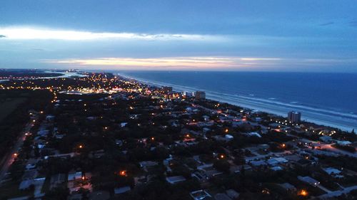 Aerial view of illuminated city by sea against sky