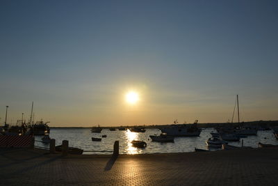 Sailboats moored at harbor against sky during sunset