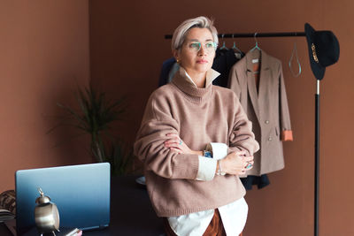 Fashion woman in brown oversize sweater and trousers standing in modern work place or office