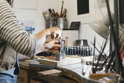 Midsection of artisan using hand tools while making jewelry on table in workshop