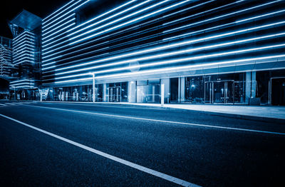 Empty road by illuminated buildings in city at night