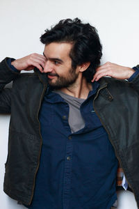 Smiling young man holding jacket against white wall