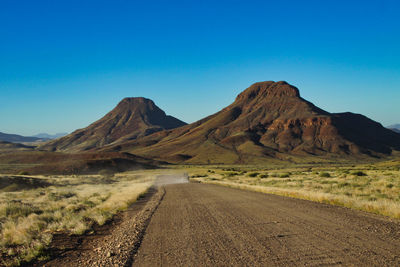 Dirt road amidst mountains against clear sky