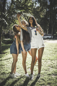 Smiling young friends taking selfie while standing on grass