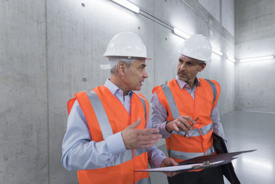 Two colleagues wearing safety vests and hard hats talking in a building