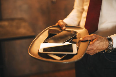 Midsection of male professional holding smart phones in tray at office