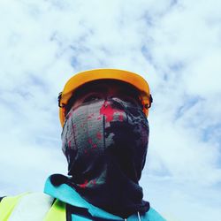 Low angle view of man wearing mask and hardhat against cloudy sky