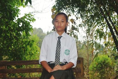 Portrait of young woman in school uniform sitting against plants