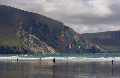 People on sea by mountains against sky