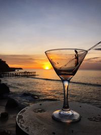 Wineglass on beach against sky during sunset