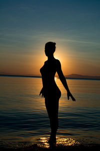 Silhouette man standing on beach against sky during sunset