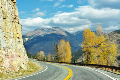 Empty road along trees and mountains against sky