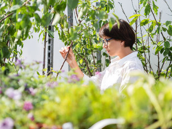 Side view of young woman standing by plants