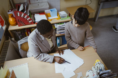 High angle view of teacher helping boy with diagram at desk in classroom