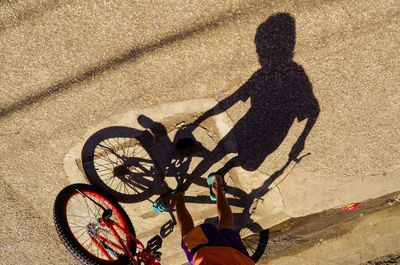 High angle view of boy with bicycle walking on road during sunny day