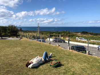 Rear view of woman sitting on beach against sky