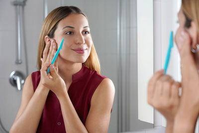 Brazilian girl shaving her face by razor at home. beautiful young woman using razor on bathroom.