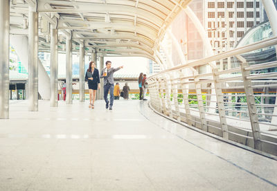 Businesswoman with colleague pointing while walking on elevated walkway in city