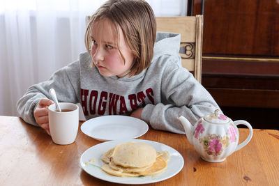 Girl eats pancakes with tea at the table