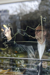 Senior businessman brainstorming, drawing formulas on window pane