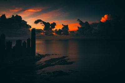 Silhouette buildings by sea against sky during sunset