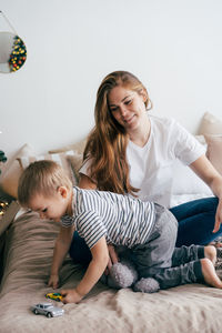 Mom with little son in the bedroom on the bed. the boy plays with toys.