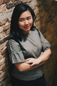 Smiling young woman looking away while leaning on brick wall