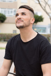 Young man looking up sitting on bench in city