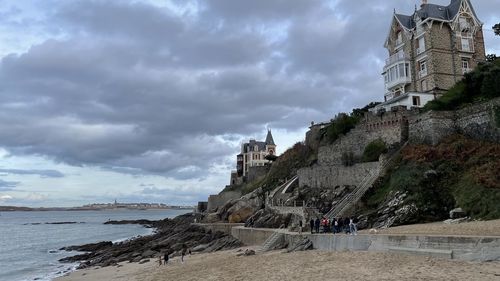 Old building by sea against cloudy sky