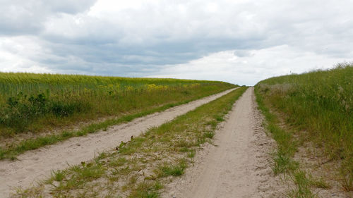 Dirt road in field against cloudy sky