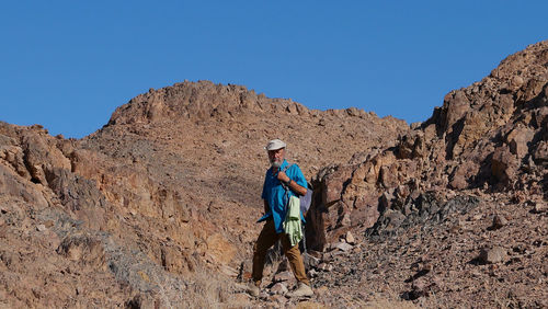 Senior man walking on mountain against clear blue sky