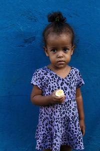 Portrait of girl holding food against blue wall