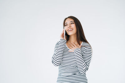 Young happy asian woman with long hair in striped longsleeve using mobile phone on white background 