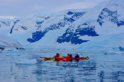 People in boat on river against snowcapped mountains