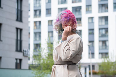 Side view of young woman standing against buildings in city