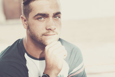 Close-up portrait of thoughtful young man with hand on chin at home