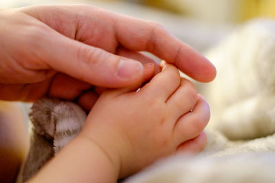 Cropped image of parent holding baby hand on bed