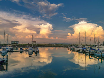 Sailboats moored at harbor against sky during sunset