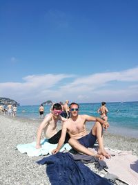 Friends sitting at beach against blue sky