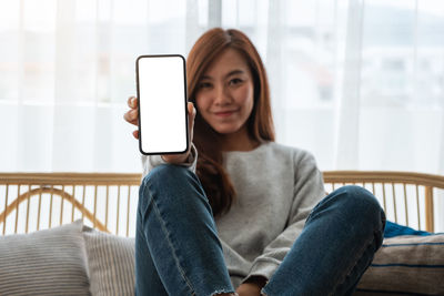 Young woman using mobile phone while sitting on sofa at home